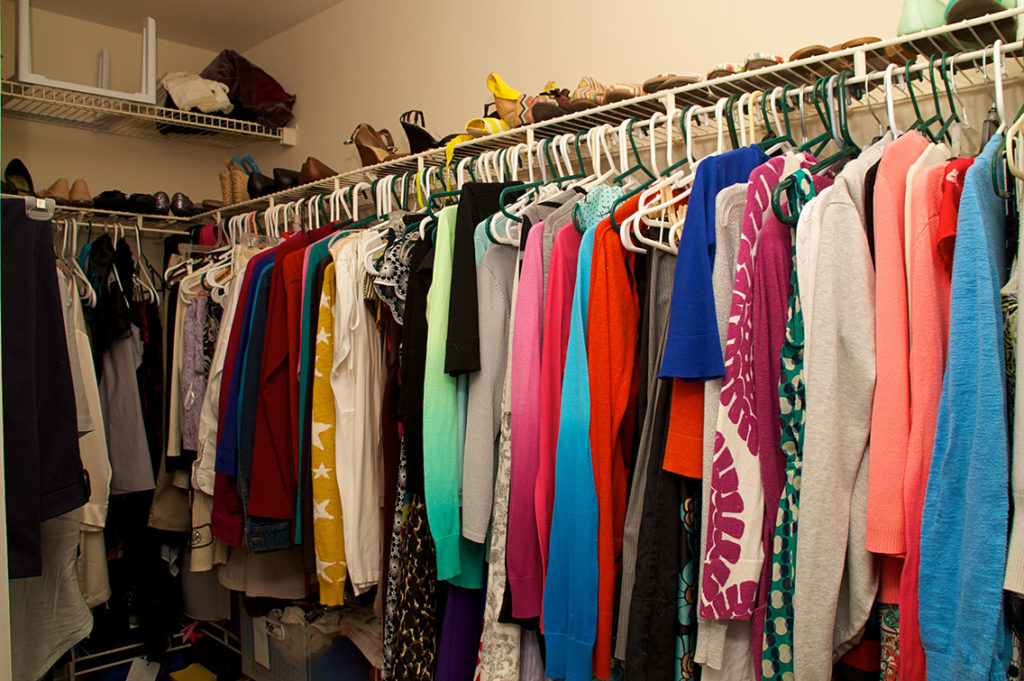 Looking into a full walk in closet belonging to a woman. Full of clothing, hangers, shelves and shoes.